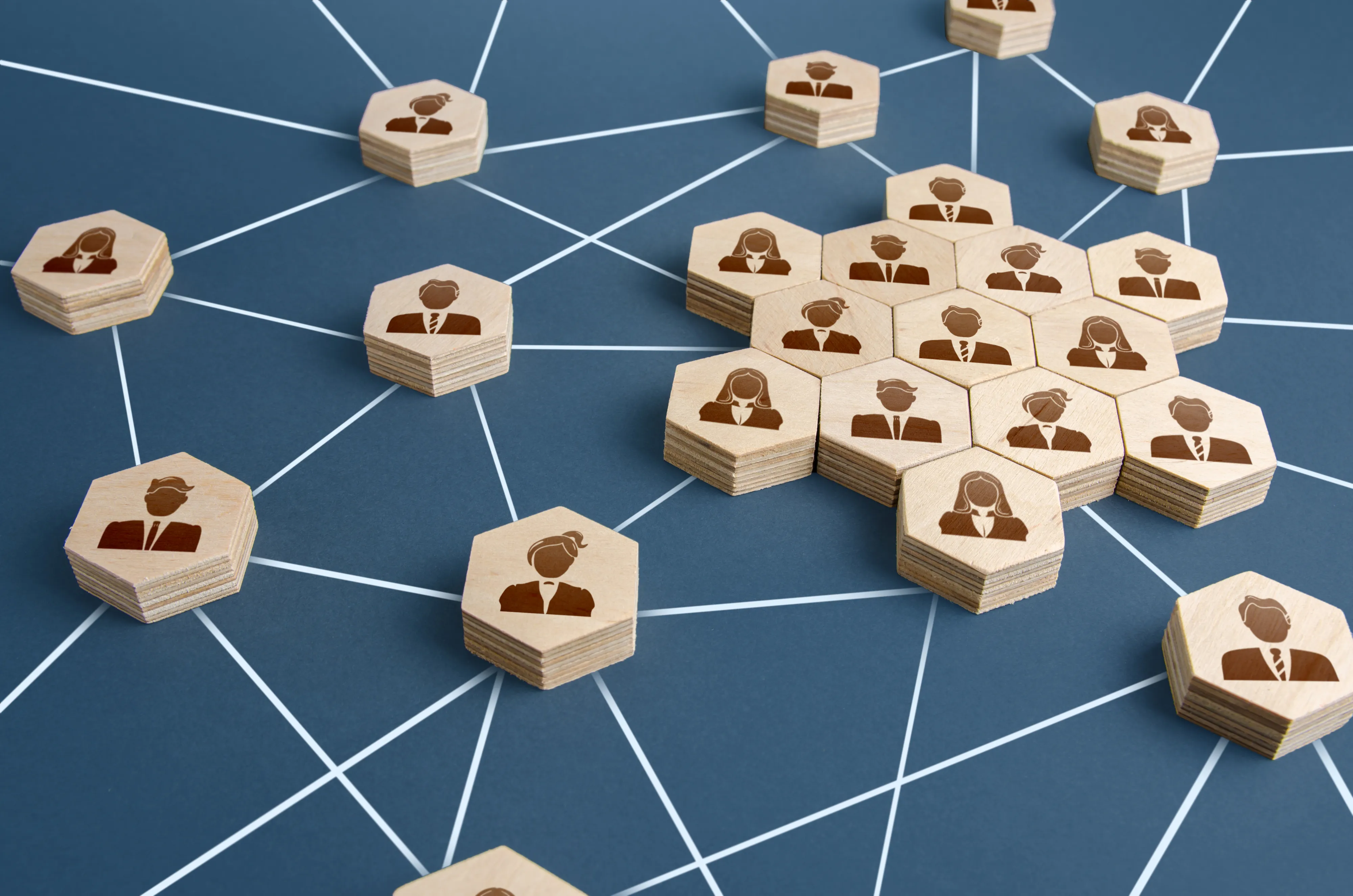 六角形のウッドブロックに描かれた人のアイコンが、白い線で相互につながれたネットワーク構造のイメージ